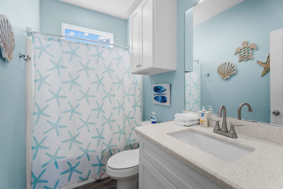 This full bathroom features a convenient vanity and a shower and tub combo, accented by colorful starfish décor, continuing the home's relaxed coastal style.