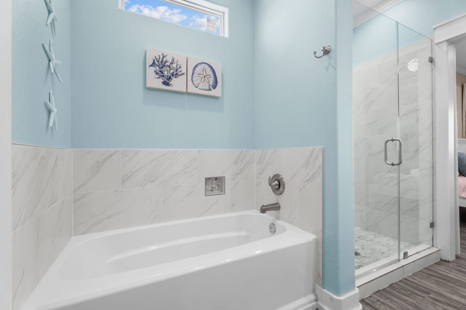 The ensuite bathroom includes a relaxing soaking tub and a separate walk-in shower, surrounded by clean finishes and subtle coastal décor.