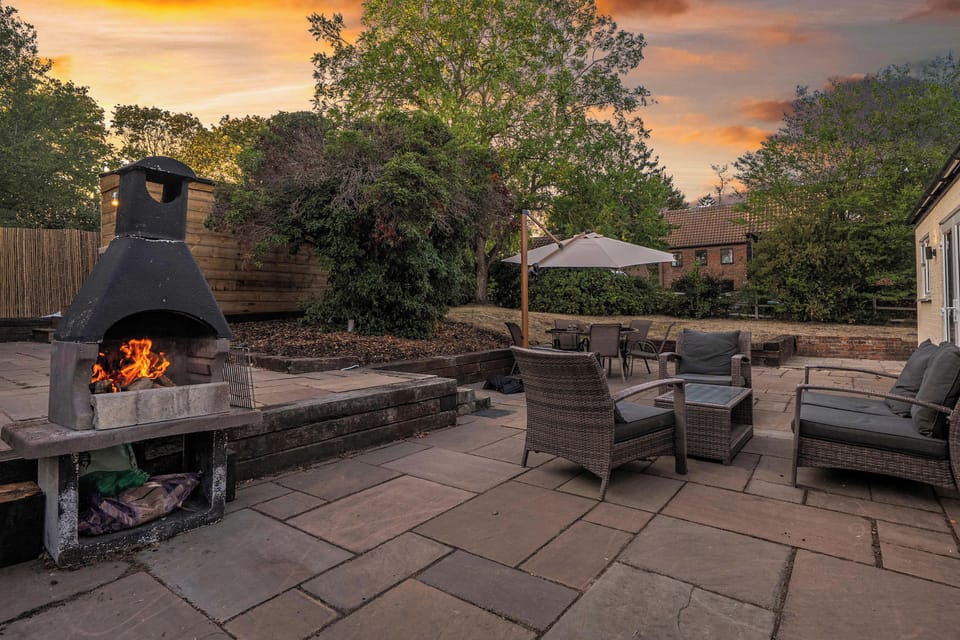 Outdoor Space: Generous patio area with comfortable rattan lounge chairs, black metal chimenea with crackling fire, natu