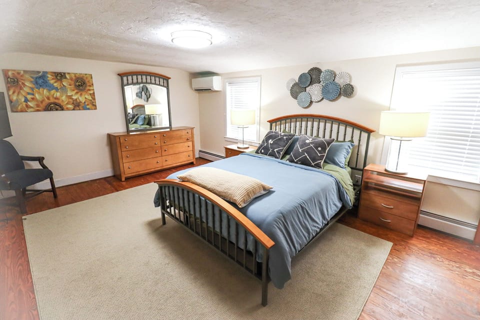 Relax in this bright and spacious bedroom featuring a comfortable queen bed, warm wood furnishings, and plenty of natural light