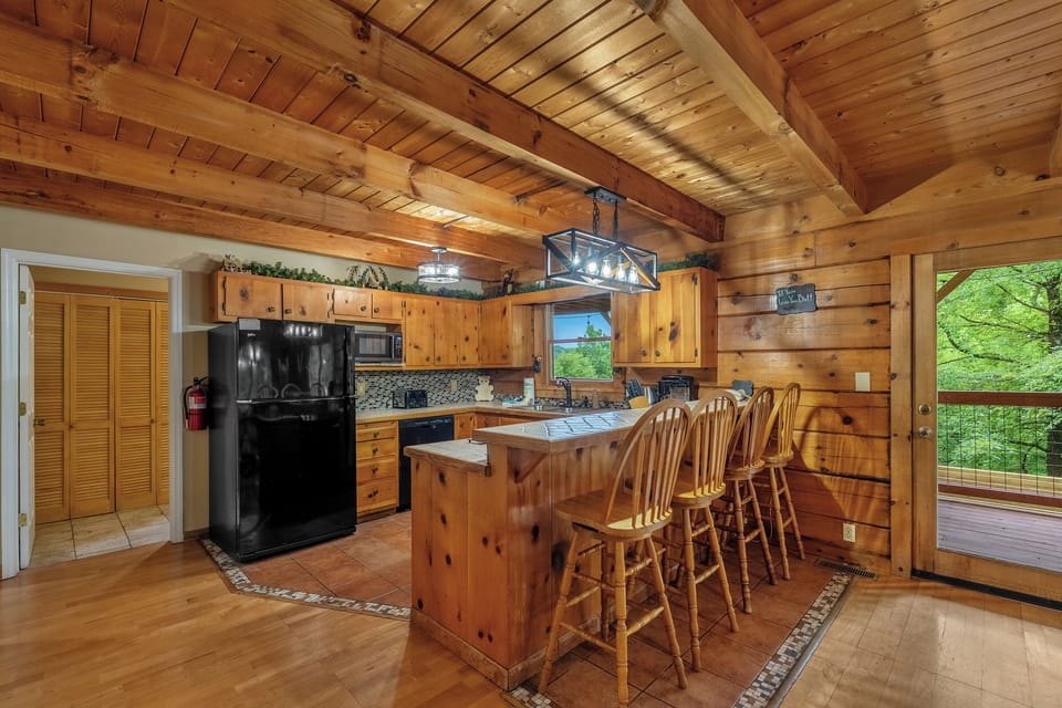 Full kitchen with island bar seating and forest through the window. Cook the group breakfast, pour the coffee, and get out the door toward the mountains early.