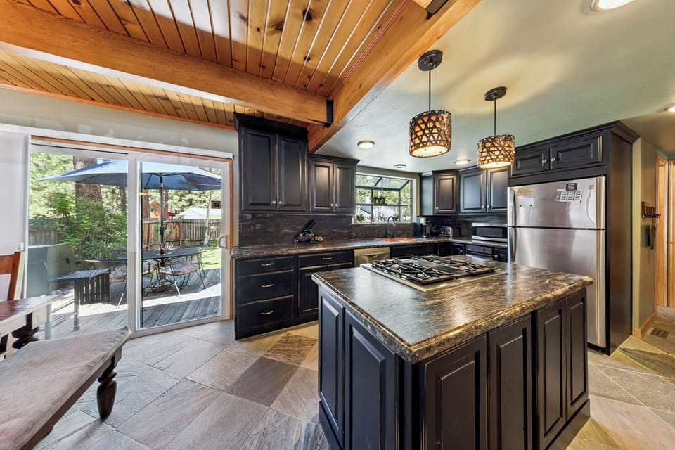 Gourmet kitchen with gas range island, wood-beamed ceilings, and pendant lighting. Glass doors open to a private patio for dining and relaxation.