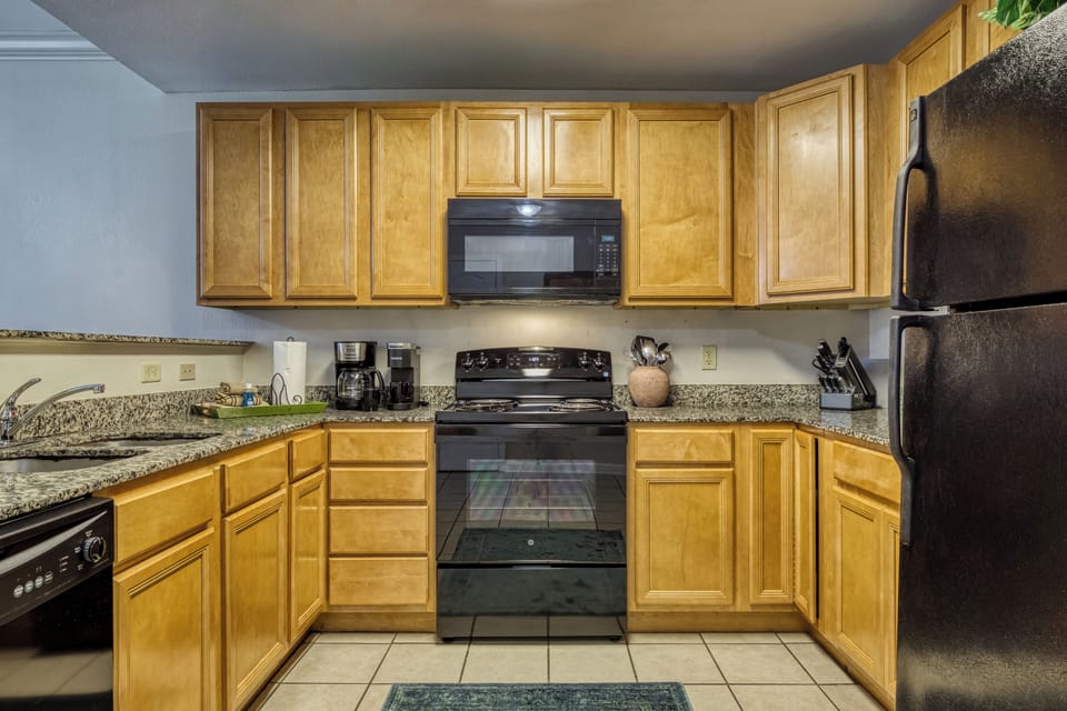 Wood cabinets, black appliances.  knives, coffee maker. kuerig, sink. utensils.
