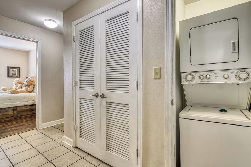 Washer and dryer, vented doors, tile floor.  two bears.  bed, door way.  picture