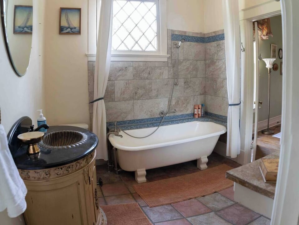 Clawfoot soaking tub with a handheld shower and terracotta tile floor