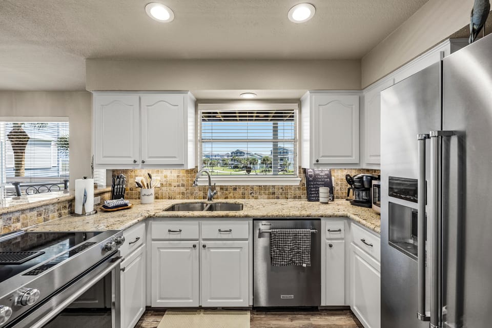 Well-equipped kitchen featuring crisp white cabinetry, stainless-steel appliances, ample counter space, and peaceful neighborhood views.