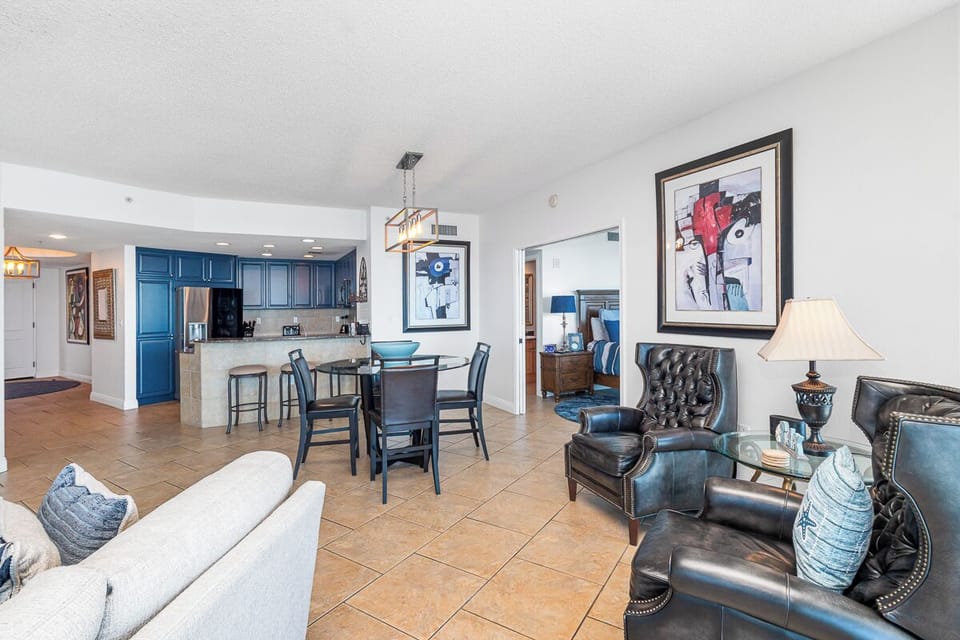 Relax in the stylish living area with plush seating and artwork, then gather at the dining table or enjoy preparing meals in your fully equipped kitchen with modern blue cabinetry.