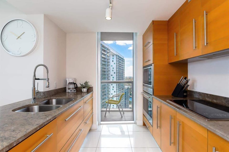 Sleek galley kitchen with granite countertops, stainless appliances, and direct balcony access — enjoy skyline views while you brew your morning coffee.