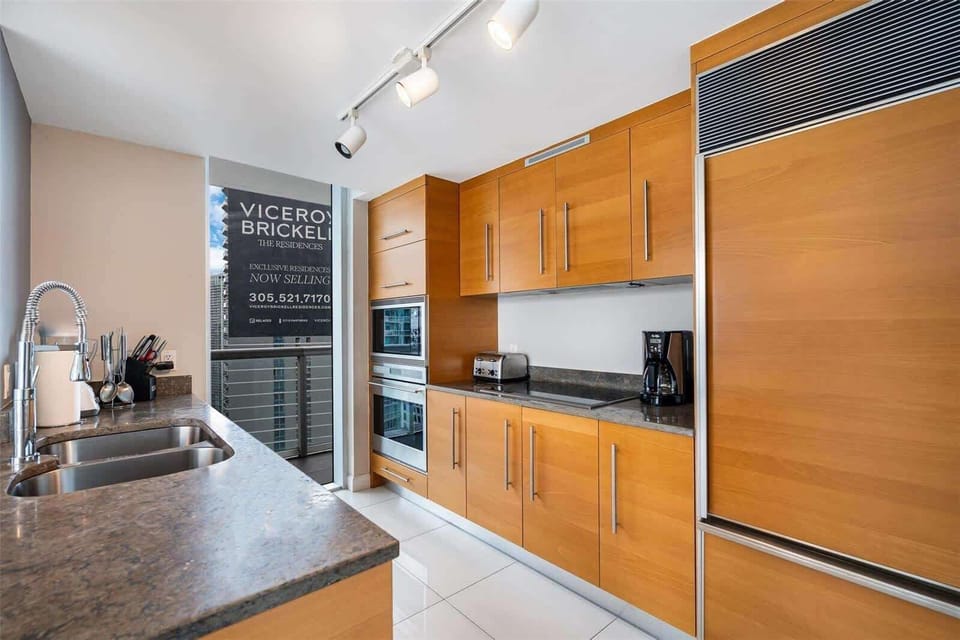 Fully stocked kitchen with granite counters, built-in stainless appliances, and warm wood cabinetry — everything you need to cook and dine in the heart of Brickell.