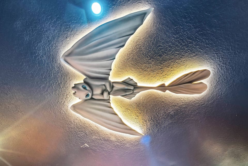 Look up to see the unique ceiling art of a stunning stylized bird, adding whimsy to the room. Soft lighting accentuates its intricate details and calming colors, instilling a sense of wonder and creativity in the space.