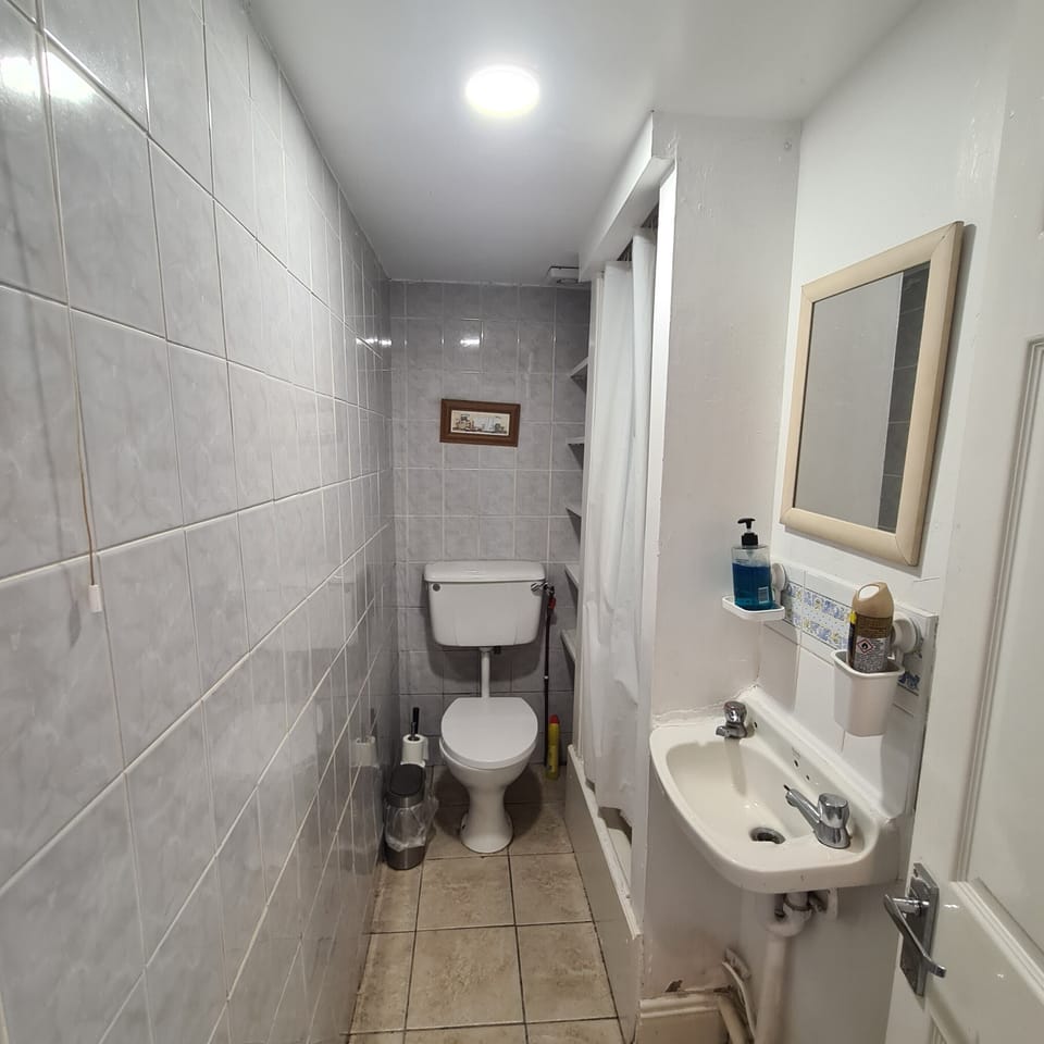 Bright tiled bathroom with shower, sink, and practical guest essentials