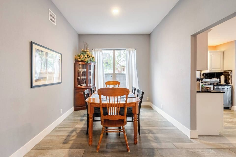 Bright dining area with a wooden table and six chairs, perfect for meals or gatherings. A large window with white curtains provides natural light, and a decorative china cabinet adds charm. Adjacent to the kitchen for convenient serving.