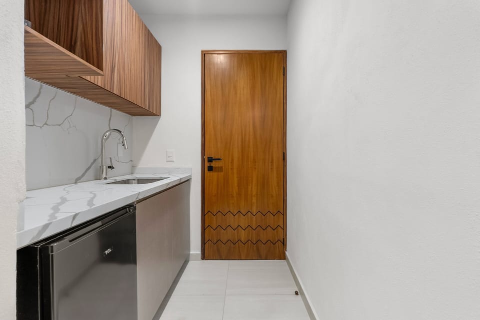 A wider view of the independent lock-off kitchenette, highlighting the premium quartz finishes, integrated mini-fridge, under-sink cabinets, and a gorgeous decorative wooden door leading out.
