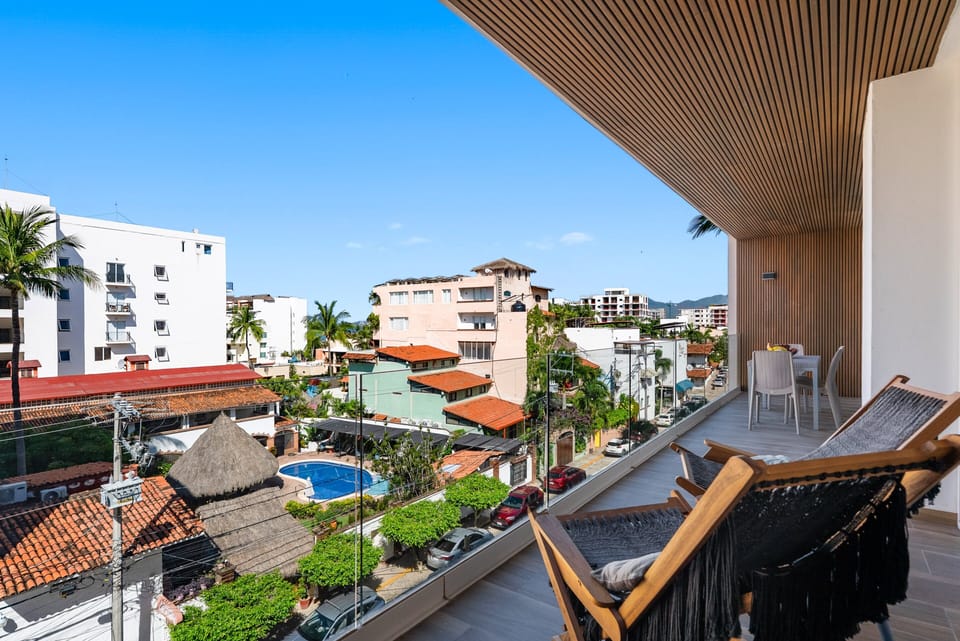 Step onto your spacious covered terrace with woven lounge seating, dining space, and glass railings overlooking lush palms and neighborhood pool views.