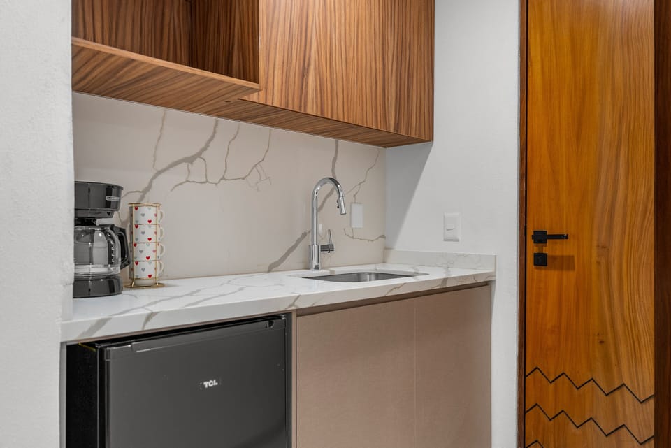 Unit 401 studio kitchenette: refined quartz-style counters, mini-fridge, coffee station, and rich parota wood cabinetry crafted for guest autonomy.
