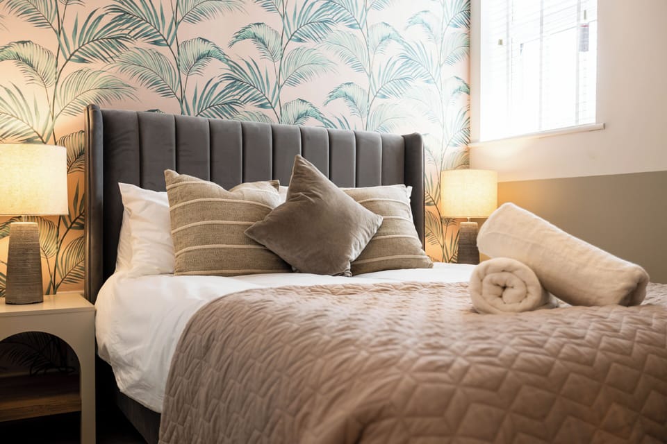 Sunny, stylish bedroom with plush bedding, palm wallpaper & soft lighting