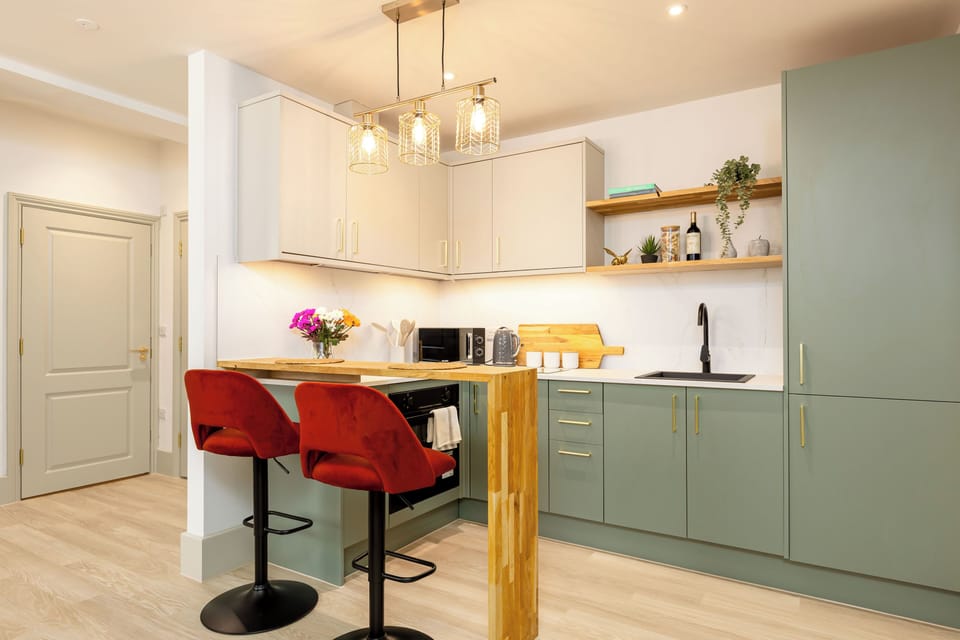 Sage-green chef’s kitchen with breakfast bar, open shelving, and pendant lights