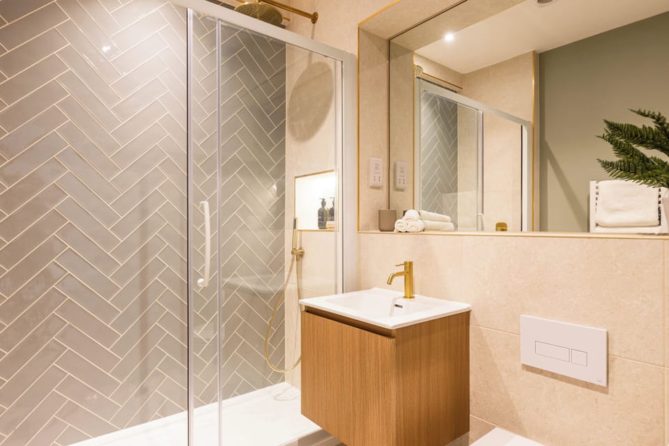 Stylish bath with rain shower, herringbone tile, gold accents, and floating vanity.