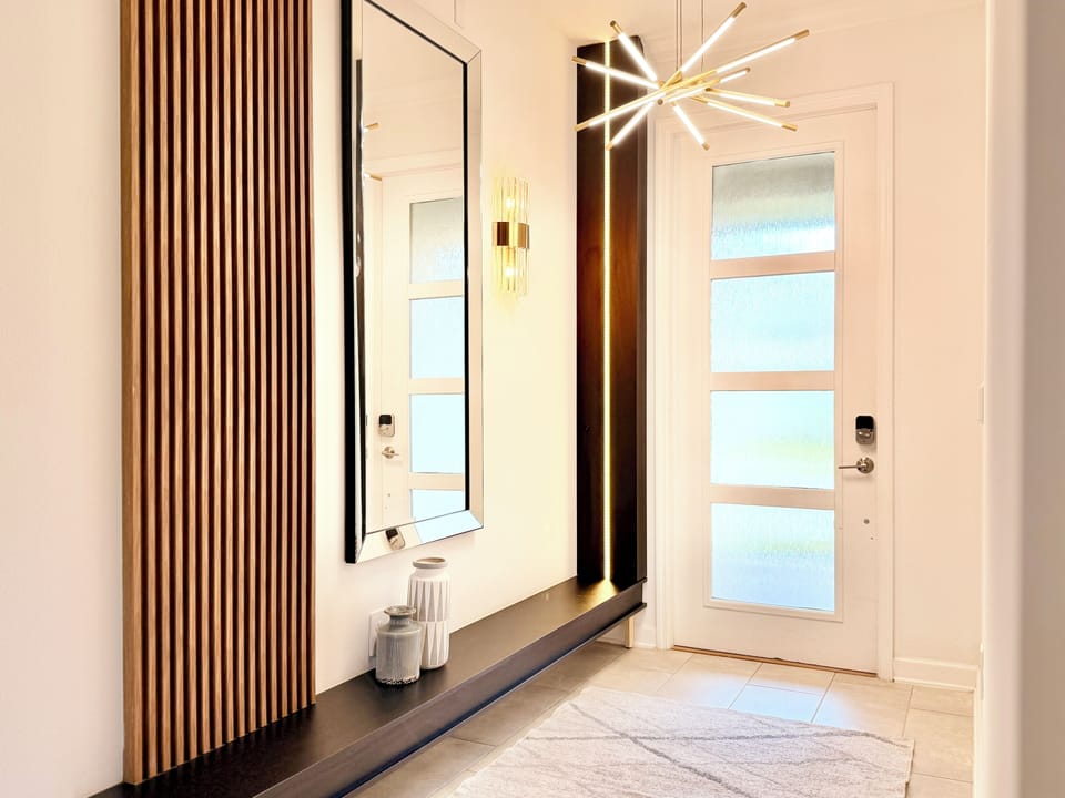 Stylish entryway with dark console, wood-slat wall, mirror & starburst lighting.