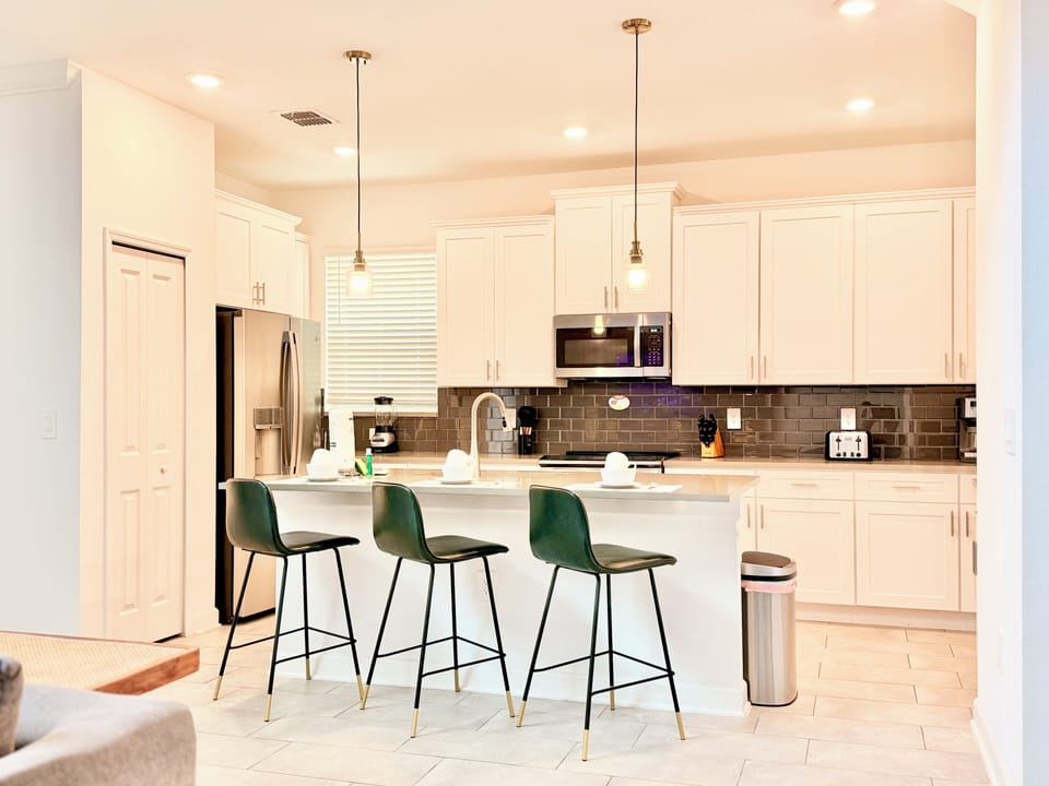 Fully equipped kitchen with white cabinetry, dark backsplash, and quartz island.