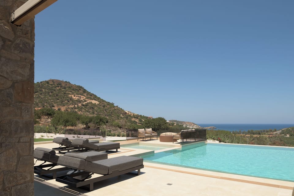 Shaded lounge areas overlook the pool, countryside, and distant Cretan Sea.
