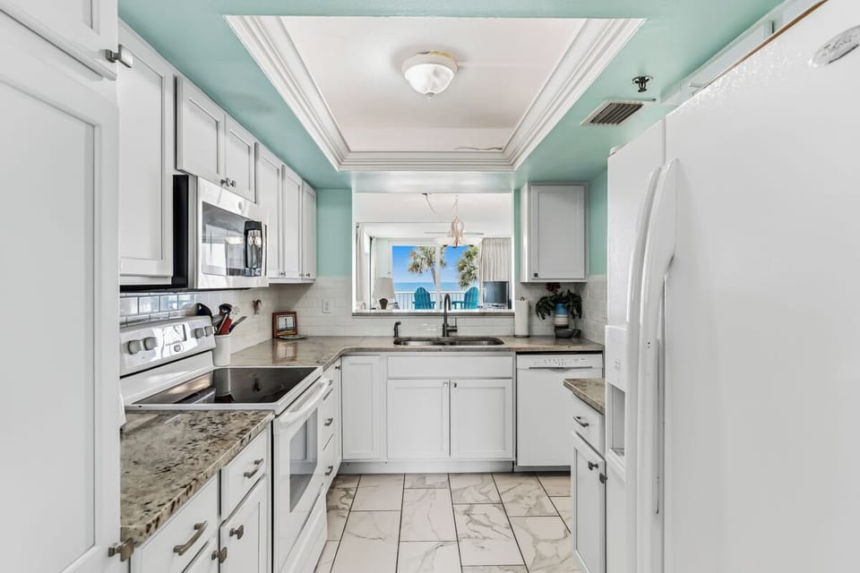 Picture yourself preparing meals in this bright, fully equipped kitchen with modern appliances and stunning ocean views just beyond the pass-through window—your perfect beachside retreat awaits.