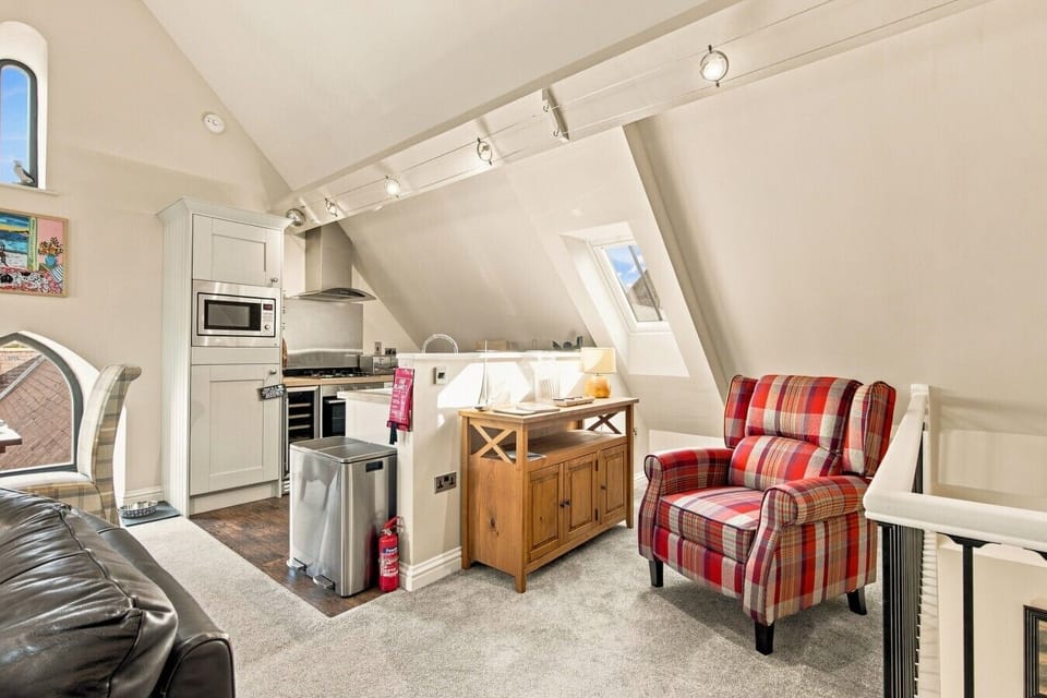 Comfortable lounge with tartan armchair and well-equipped kitchen beyond.