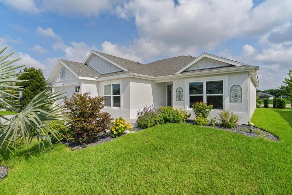 This beautifully landscaped single-story home sits on a lush green lawn with vibrant garden beds and tropical plants, offering a welcoming arrival to your vacation retreat.