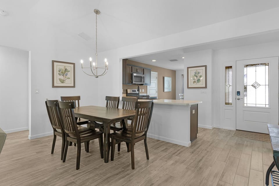 Your dining space flows seamlessly into an open kitchen, where warm wood tones meet clean white finishes. Gather around the table under elegant chandelier light and enjoy easy access to everything you need.