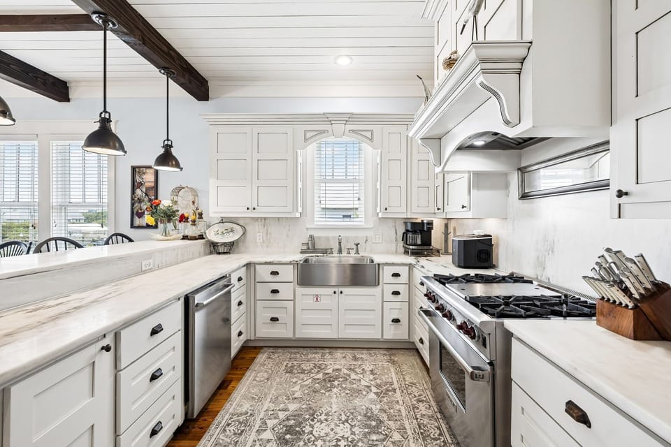 Step into your gourmet kitchen with gleaming marble counters, a professional-grade gas range, and charming pendant lights overhead. Exposed beams and elegant cabinetry create a warm, inviting space for cooking and gathering.