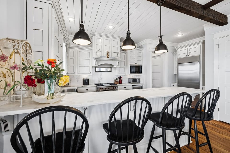 Step into your gourmet kitchen where rustic wooden beams meet elegant white cabinetry. The spacious marble island invites you to gather with friends, while fresh flowers add a welcoming touch to your home away from home.