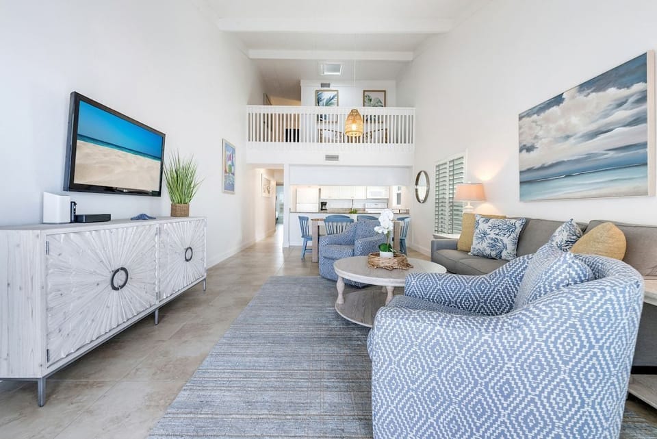 Another view of the open-concept living area shows coastal décor, comfortable seating, a TV, and views of the kitchen and loft.