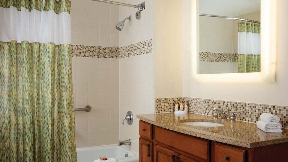 Bright bathroom with granite vanity, tub-shower combo, and warm finishes