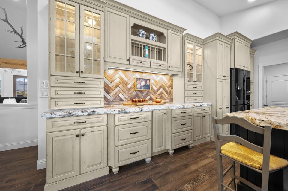 Detailed cabinetry, illuminated glass-front storage, elegant hardware, and a patterned backsplash give the kitchen a distinctive, upscale character.