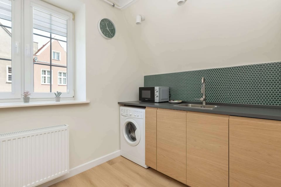 A bright kitchen area with ample counter space and a washing machine. The large window brings in plenty of natural light.