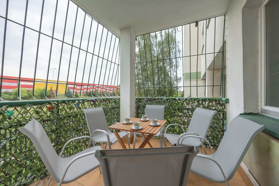 A covered balcony features a table and comfortable chairs for outdoor dining or relaxation. Greenery surrounds the space, creating a pleasant setting.
