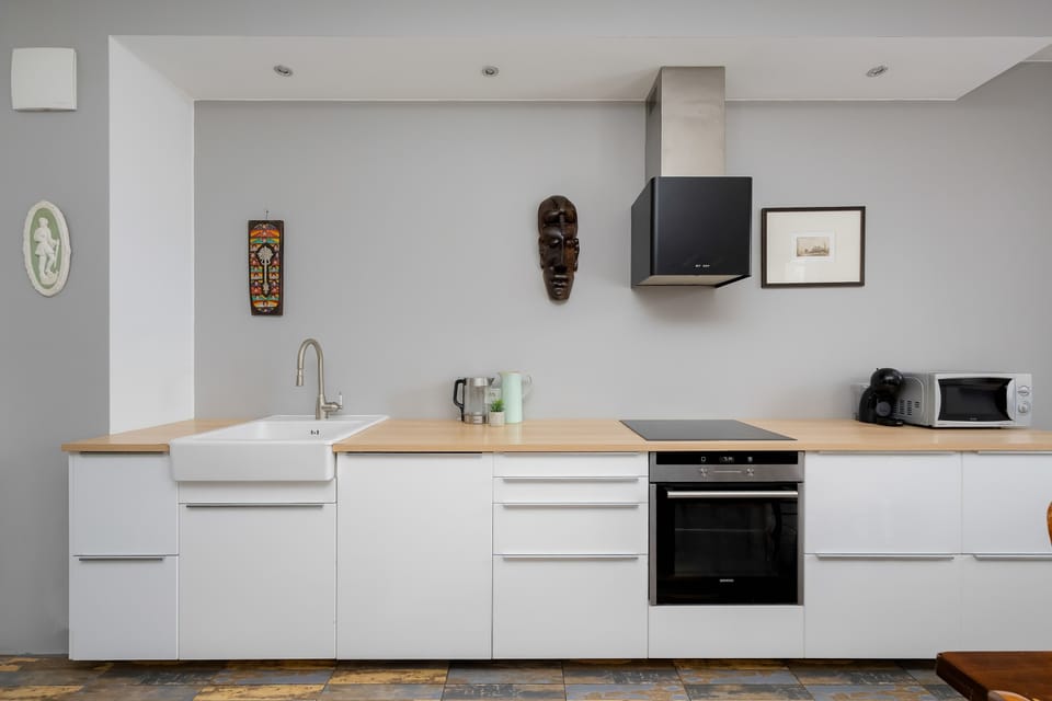 A modern kitchenette is fitted with sleek white cabinetry and a light wooden countertop. An integrated oven and stove top are visible, along with decorative items on the counter and wall.