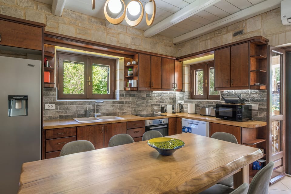 Step into your beautifully appointed kitchen where natural light floods warm wood cabinetry and natural stone accents, inviting you to prepare meals in this welcoming, fully equipped space.