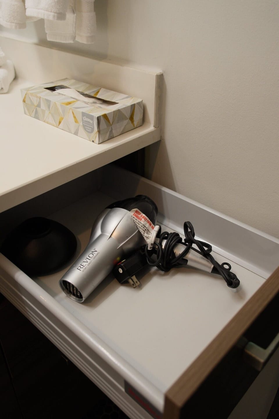Unique apartment bathroom drawer holding a Revlon hair dryer, with a tissue box sitting on the counter above.