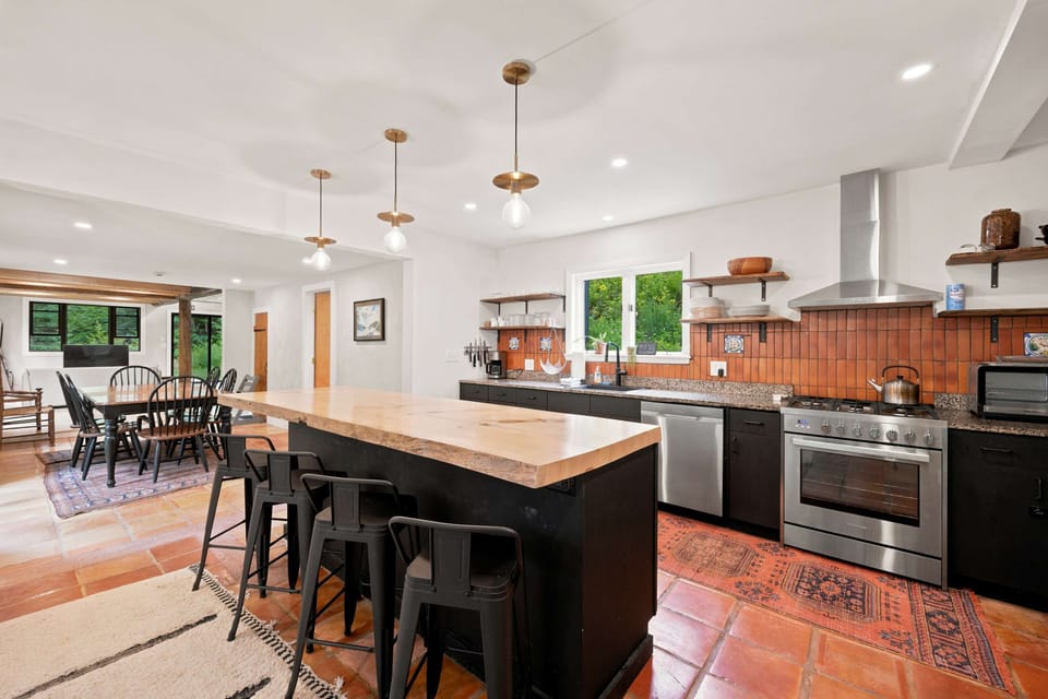 The open kitchen and dining area come together with terracotta tile, a brick backsplash, and an island with seating for morning coffee before you head out.