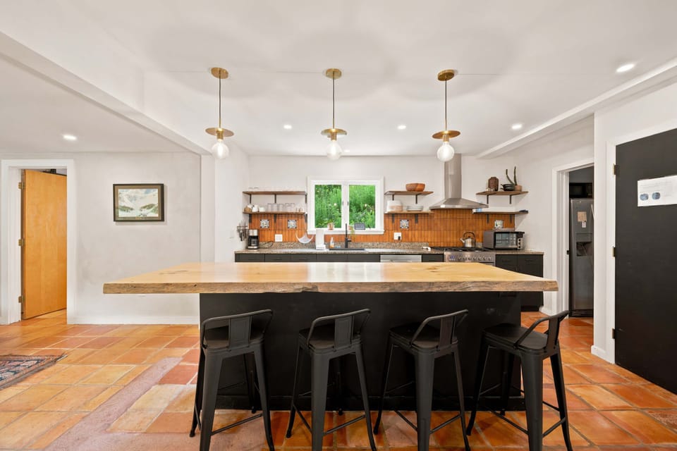Gather around the wooden island with seating while you cook, with pendant lights overhead and windows framing the greenery.
