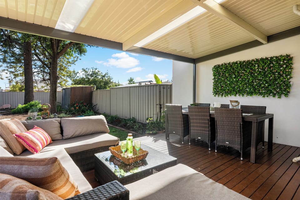 Stretch out with a drink on the cushioned outdoor lounge, where the covered deck offers shade and an open outlook across the leafy backyard.