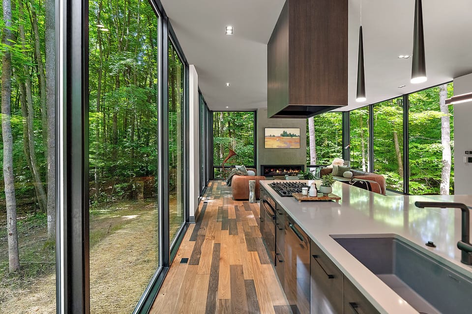 Modern glass-walled retreat with forest views, luxe kitchen, and fireplace