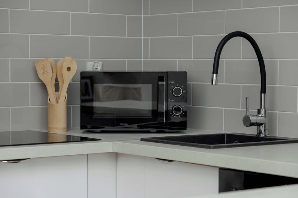 Kitchen worktop with a microwave, black sink, wooden utensils, and modern fittings.