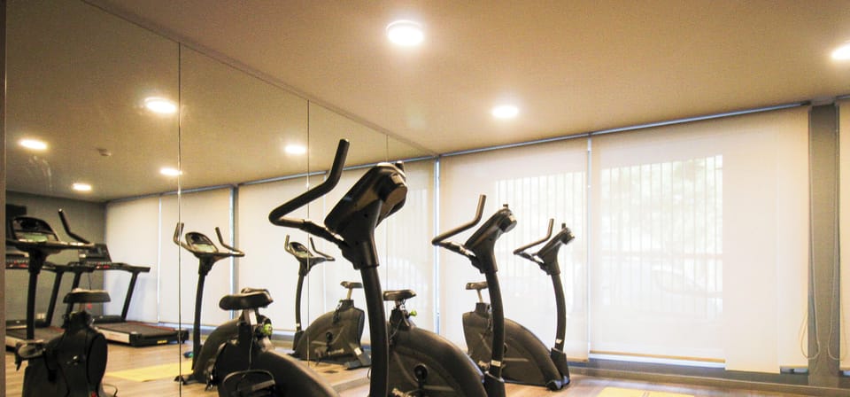 Bright on-site gym with bikes, treadmill, mirrors, and workout space