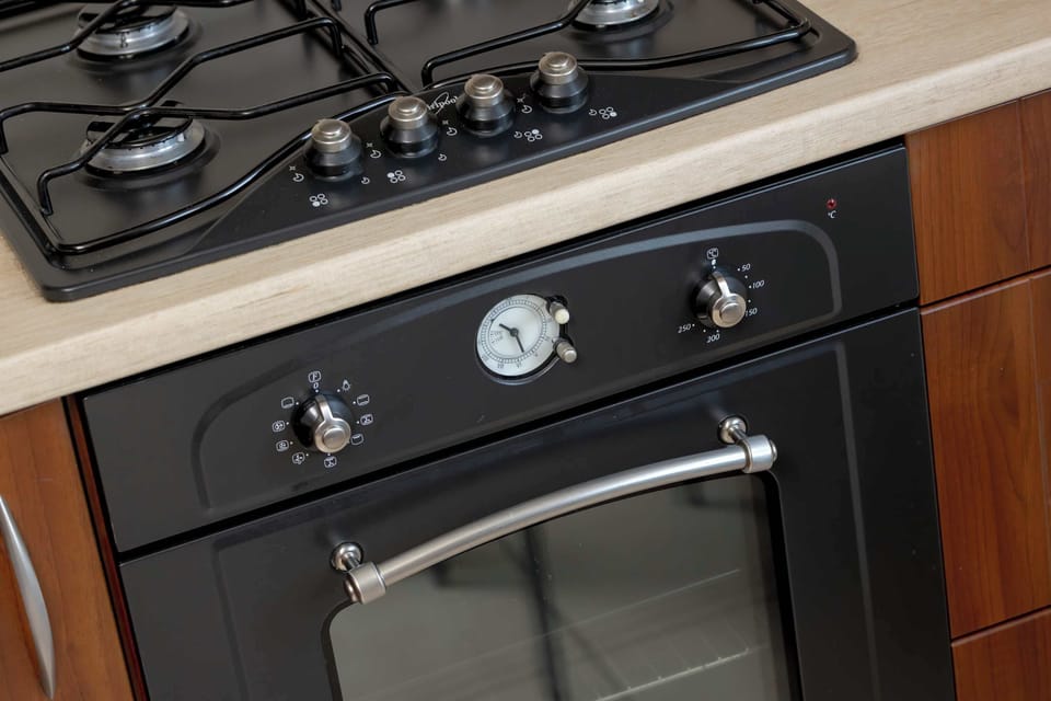 A detailed close-up shot of a modern built-in kitchen stove top and black oven with simple control knobs. The clean countertop reflects a well-maintained cooking space.