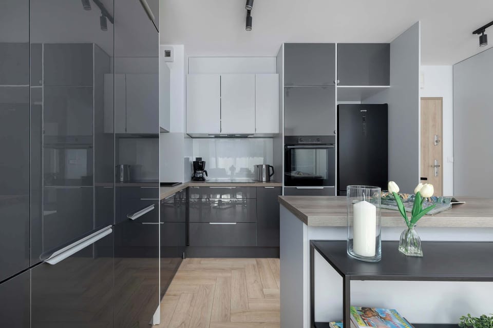 A contemporary kitchenette boasts contrasting dark grey and white cabinetry along with built-in appliances. A kitchen island provides additional counter space.