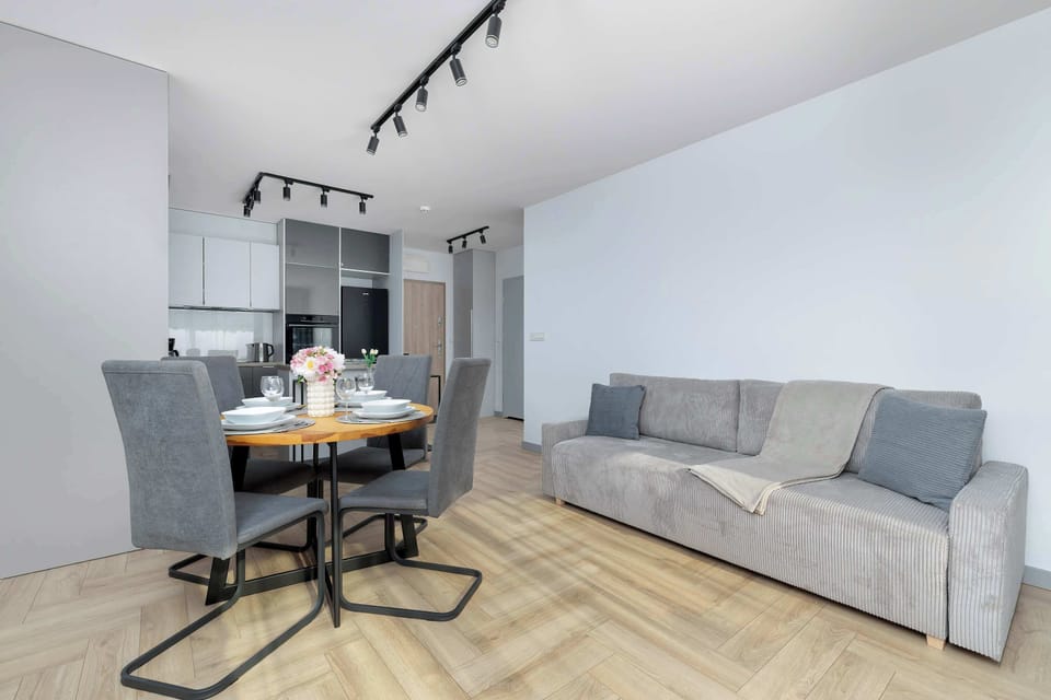 A grey sofa sits prominently in the living area.. The round dining table with dark chairs provides a central gathering spot in the open-concept room.