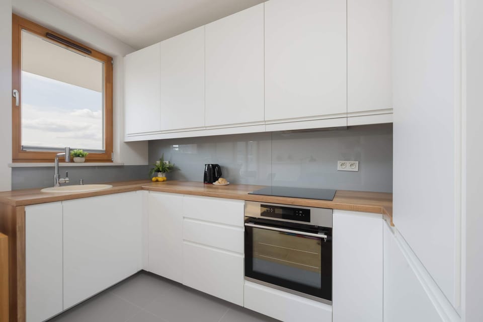 A modern white kitchen with sleek cabinets, a built-in oven, a cooktop, and a window above the countertop.