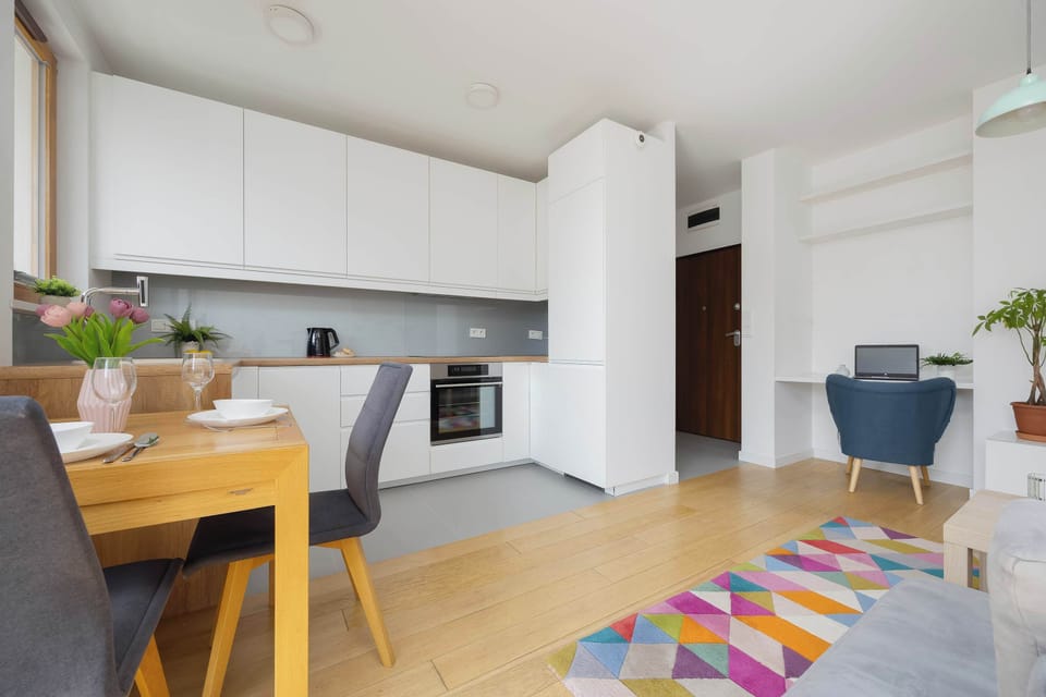 An open kitchen connected to the dining area, featuring white cabinets, modern appliances, and a colorful rug extending into the living room.